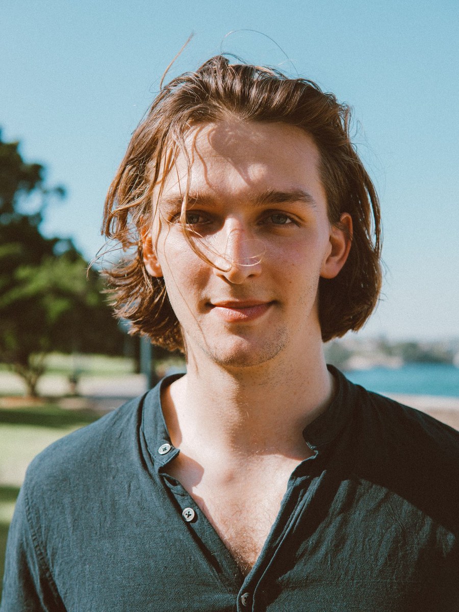 A young man smiling outdoors near water.