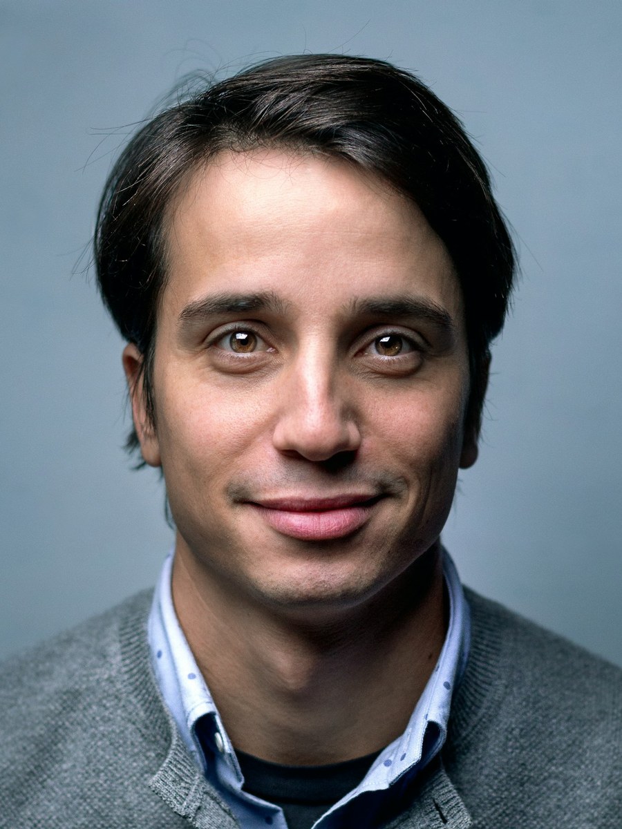 A man in a grey sweater smiling toward the camera.