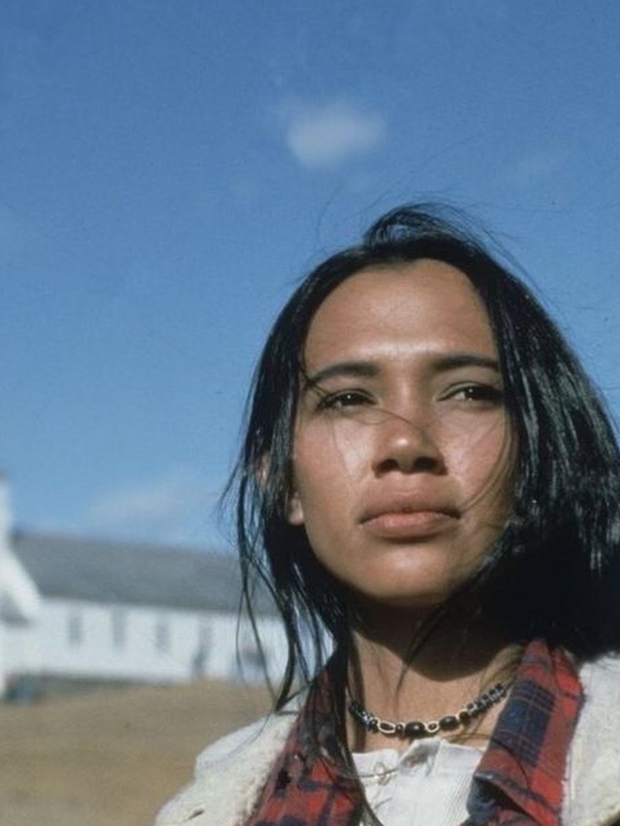 A woman in a flannel shirt and jacket outdoors.