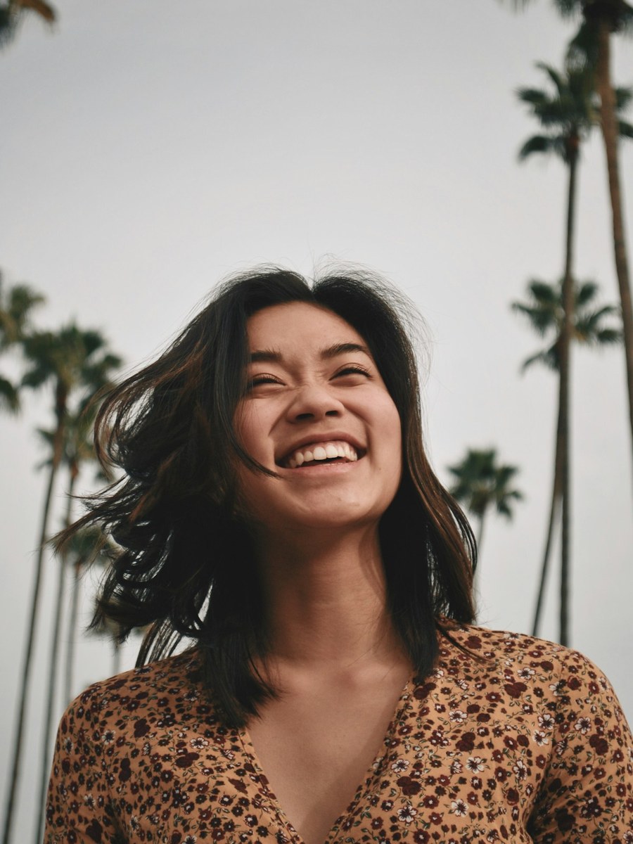 A woman laughing outdoors under palm trees.