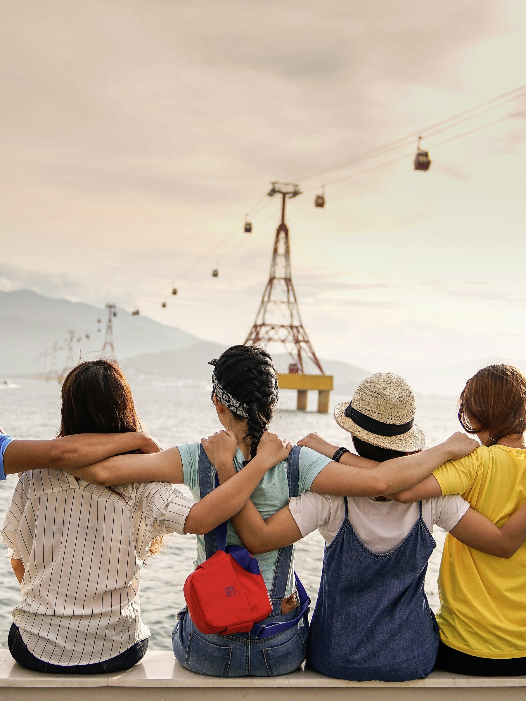 Four friends sitting together overlooking the water, arms around one another.