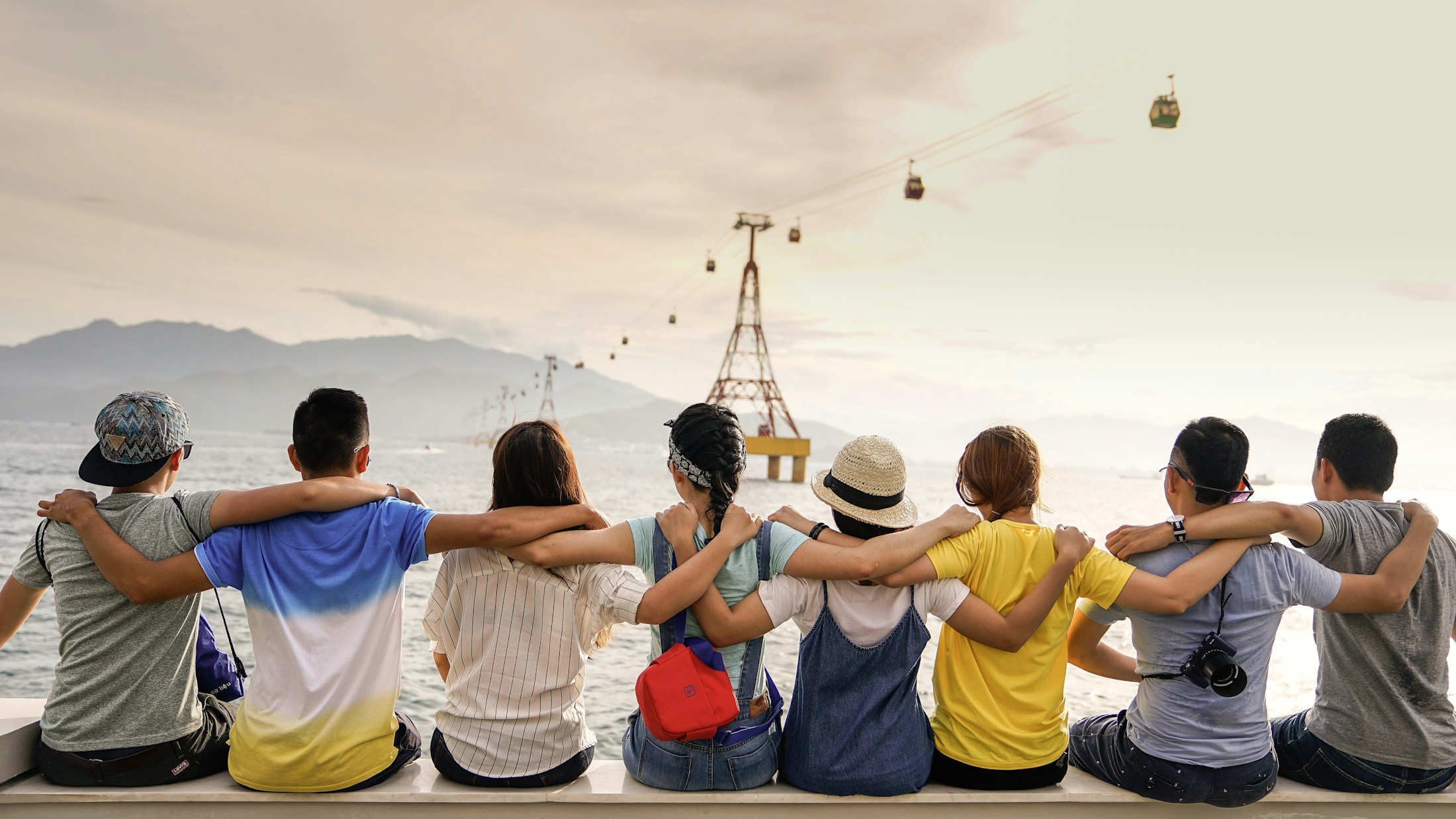 Friends sitting together with their arms around one another, looking out over the water.